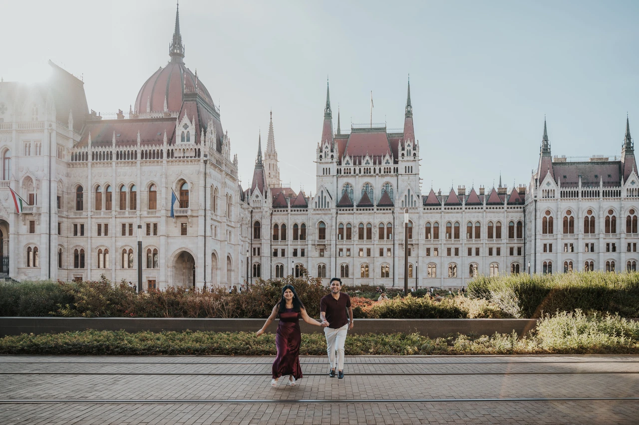 Parliament’s grand façade at a Budapest couple photoshoot A wide view of the couple walking across the paved square with Parliament’s long façade in the background during their couple photoshoot in Budapest.