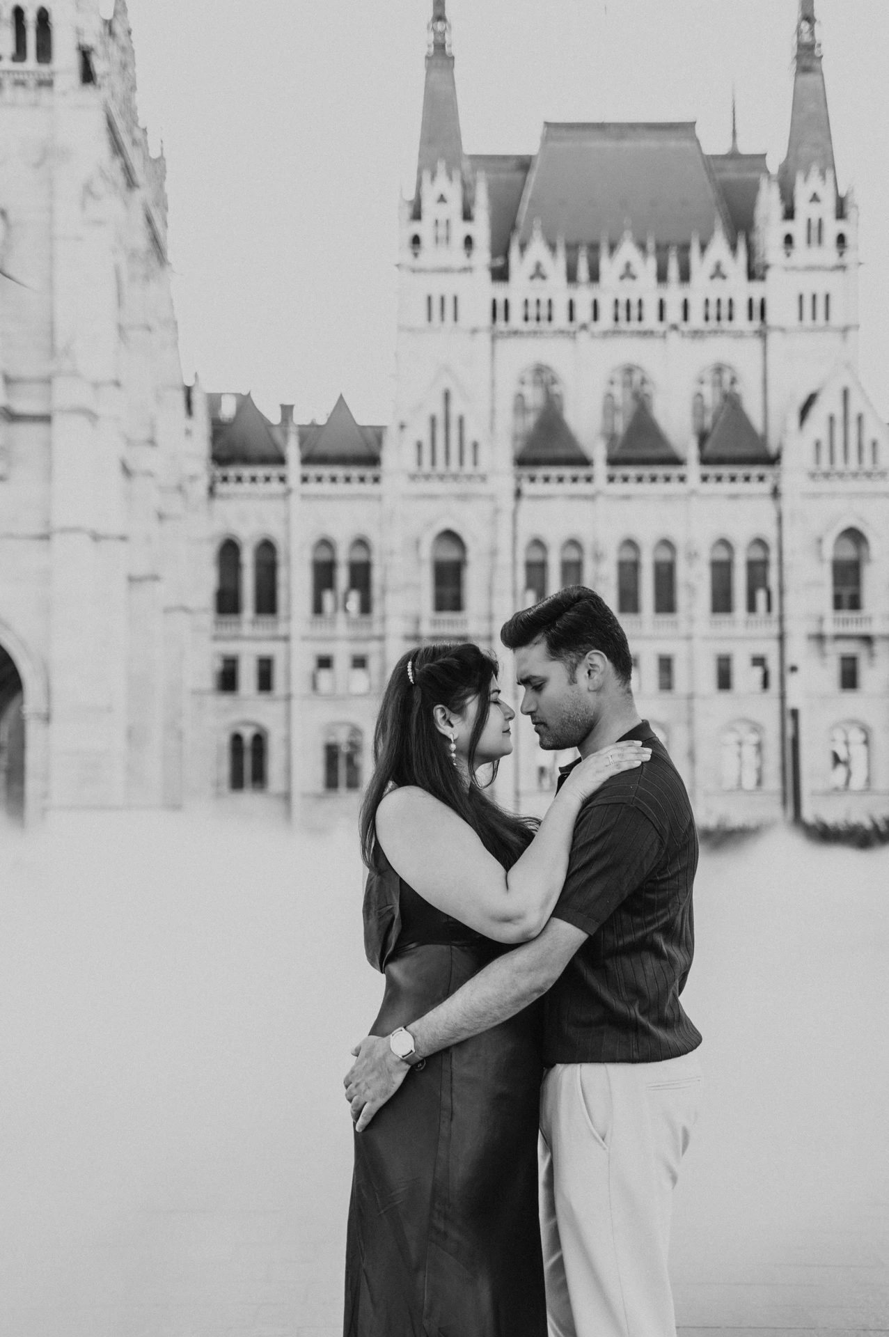 Black-and-white portrait of the couple holding one another beside Parliament with soft mist around them during their Budapest couple photoshoot.