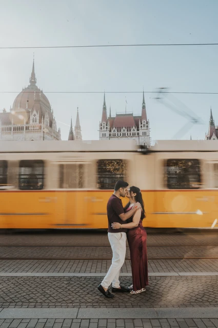 A passing yellow tram at a Budapest couple photoshoot The couple embracing beside the tracks as a yellow tram passes in front of Parliament during their Budapest couple photoshoot.
