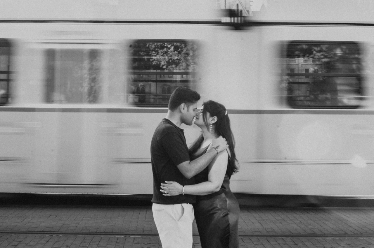 A Budapest couple photoshoot beside the tram in black and white Black-and-white landscape portrait of the couple embracing with a passing tram behind them during their Budapest couple photoshoot.