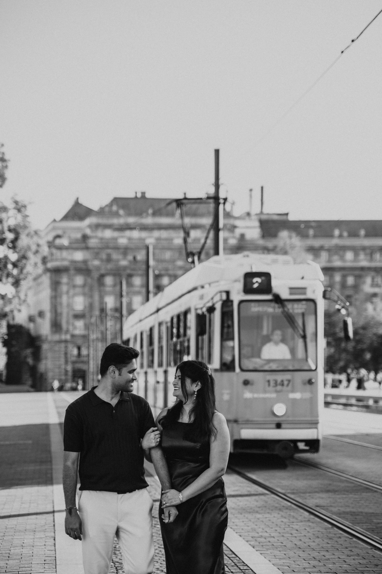 Black-and-white portrait of the couple walking in front of a tram during their Budapest couple photoshoot.