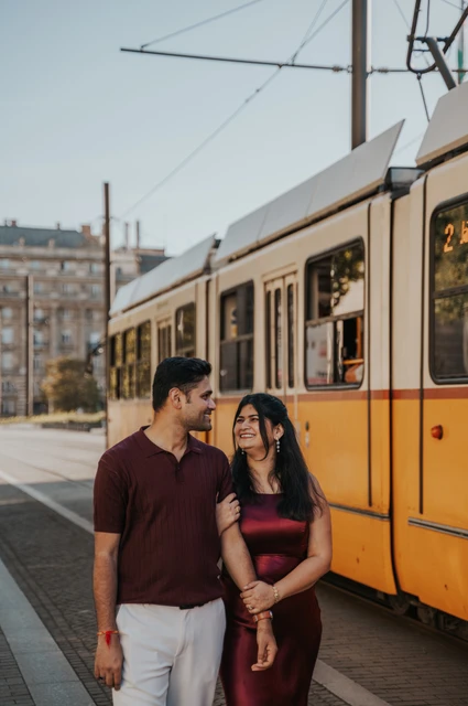 The couple walking beside the side of a yellow tram, smiling at one another during their couple photoshoot in Budapest.