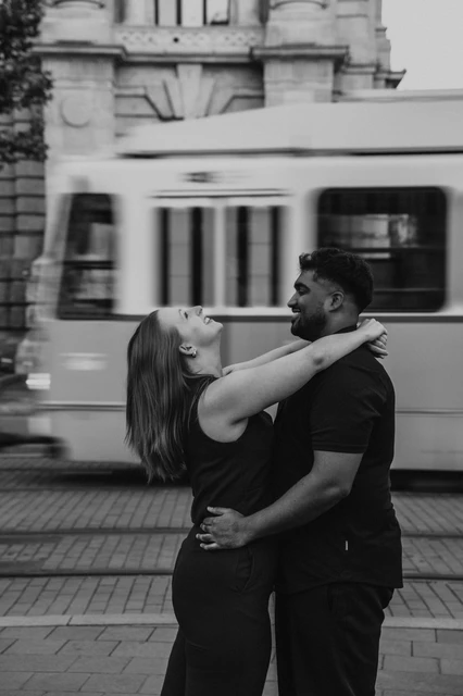 Budapest couple photoshoot: a black-and-white moment of laughter Black-and-white photograph of her leaning back laughing in his arms beside the passing Budapest tram during their Budapest couple photoshoot.