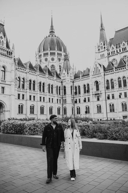 Budapest couple photoshoot: a black-and-white walk outside Parliament Black-and-white photograph of the couple walking side by side in front of the Hungarian Parliament and its flowerbeds during their Budapest couple photoshoot.