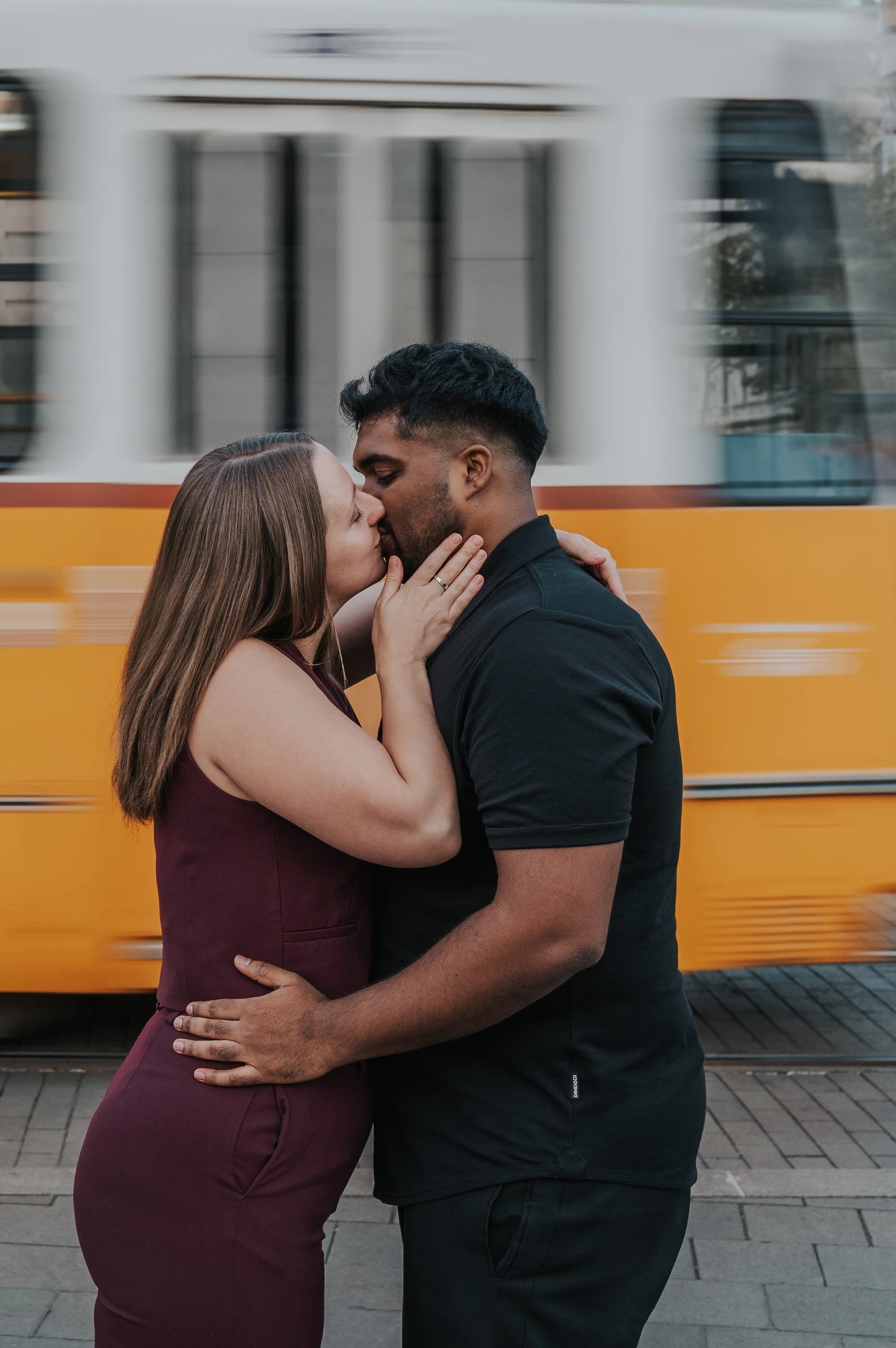 A close portrait of the couple kissing, with her hand against his cheek and a yellow tram blurred behind them during their Budapest couple photoshoot.