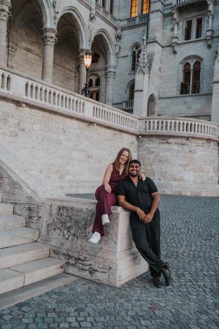 Budapest couple photoshoot: a kiss beside Parliament’s stone stairway The couple kissing beside the low stone pillar at Parliament’s staircase, with the ornate façade above them during their Budapest couple photoshoot.