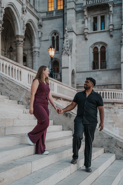Budapest couple photoshoot: a smile across the stone steps The couple smiling at one another while holding hands on different steps of Parliament’s broad staircase during their Budapest couple photoshoot.