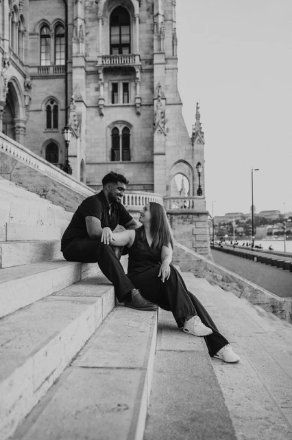 Budapest couple photoshoot: black-and-white closeness beside Parliament Black-and-white view of the couple leaning towards one another on Parliament’s broad stone steps during their Budapest couple photoshoot.