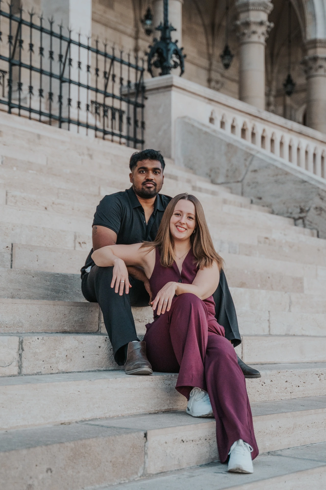 The couple seated together on Parliament’s broad stone staircase, with the carved façade and black iron railings behind them during their Budapest couple photoshoot.