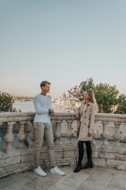 A portrait on the castle terrace at a Budapest couple photoshoot A full-length portrait of the couple standing beside a stone balustrade overlooking Budapest from Buda Castle during their couple photoshoot in Budapest.