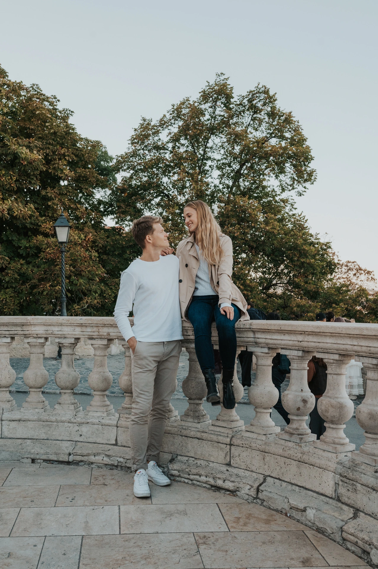 The couple walking hand in hand beside a curved stone balustrade at Buda Castle during their couple photoshoot in Budapest.