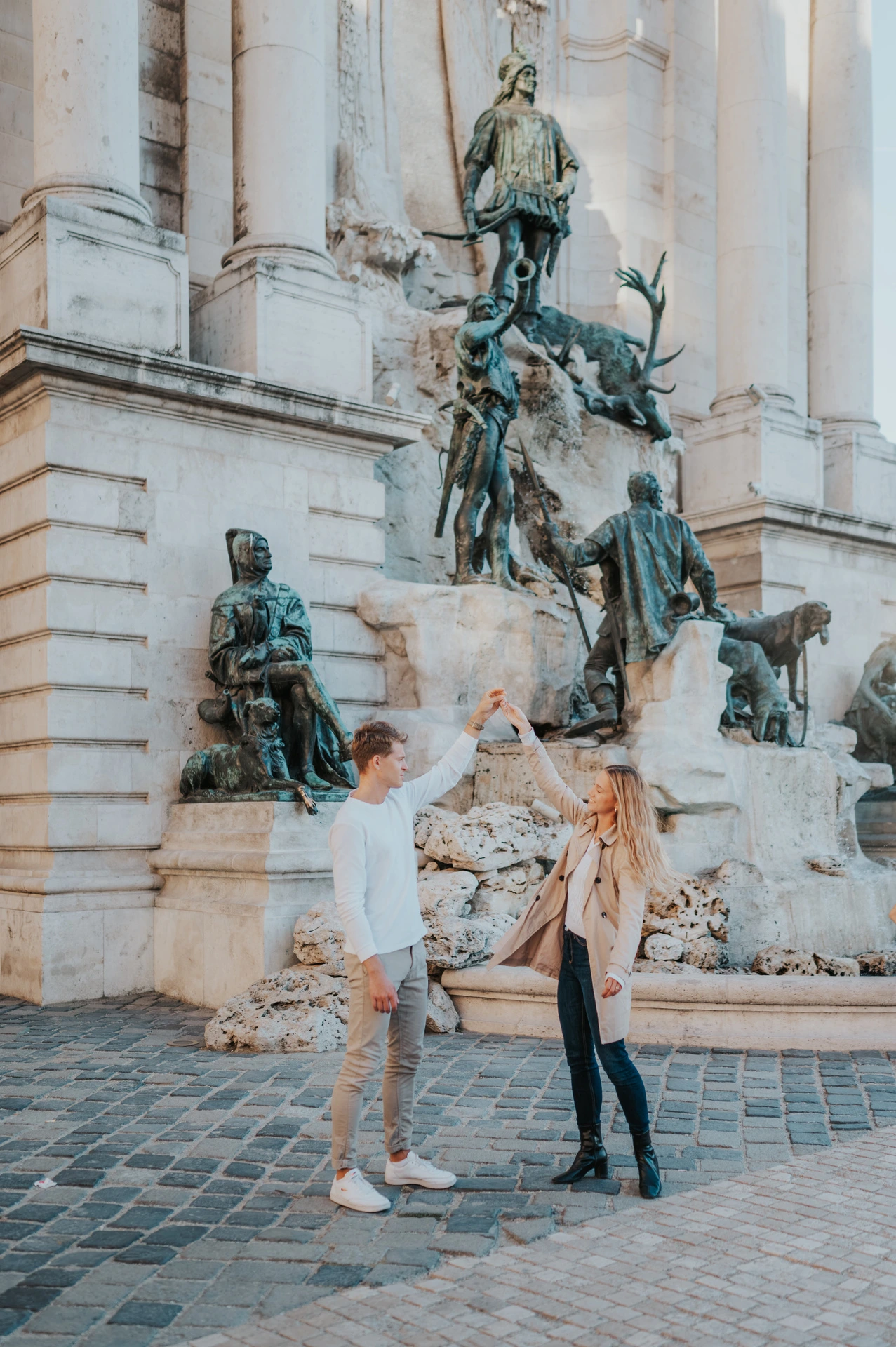 The couple sharing a playful portrait beside the bronze figures of Buda Castle’s fountain during their couple photoshoot in Budapest.