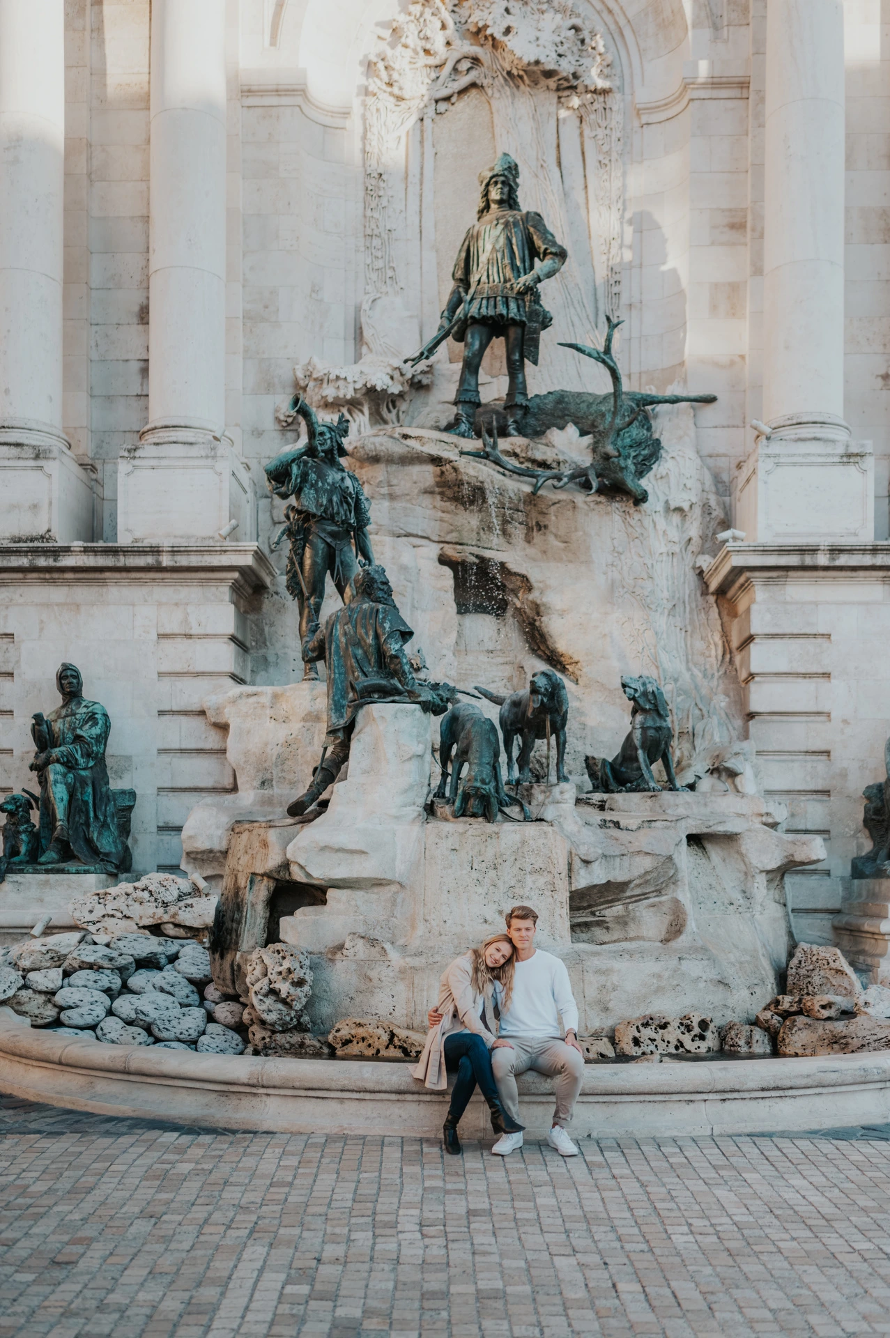 The couple sitting together at the base of Buda Castle’s large sculpted fountain during their couple photoshoot in Budapest.