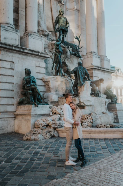 The couple embracing in front of the bronze figures and carved stone at Buda Castle’s fountain during their couple photoshoot in Budapest.