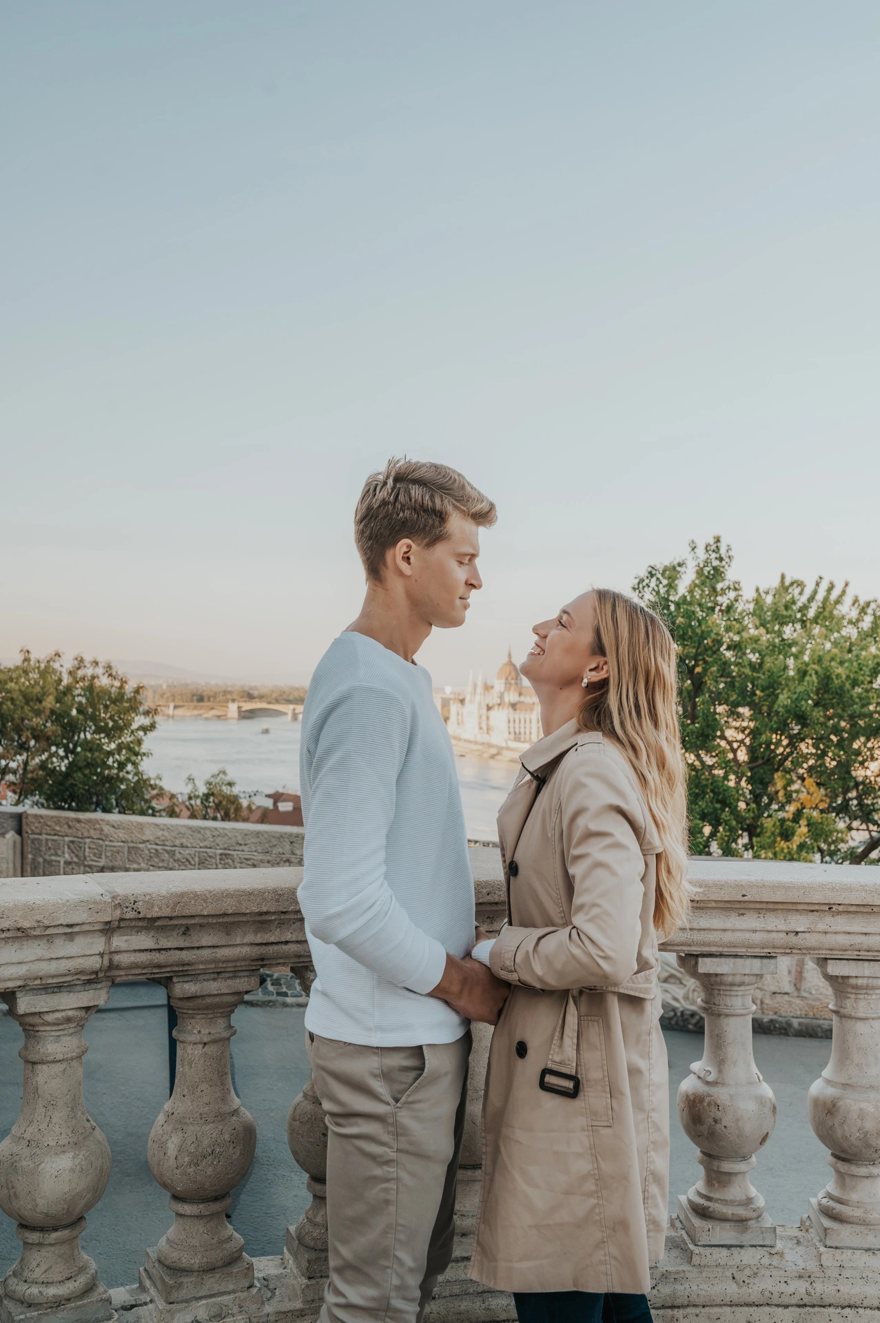 The couple embracing face to face beside Buda Castle’s stone balustrade with the city in the background during their couple photoshoot in Budapest.