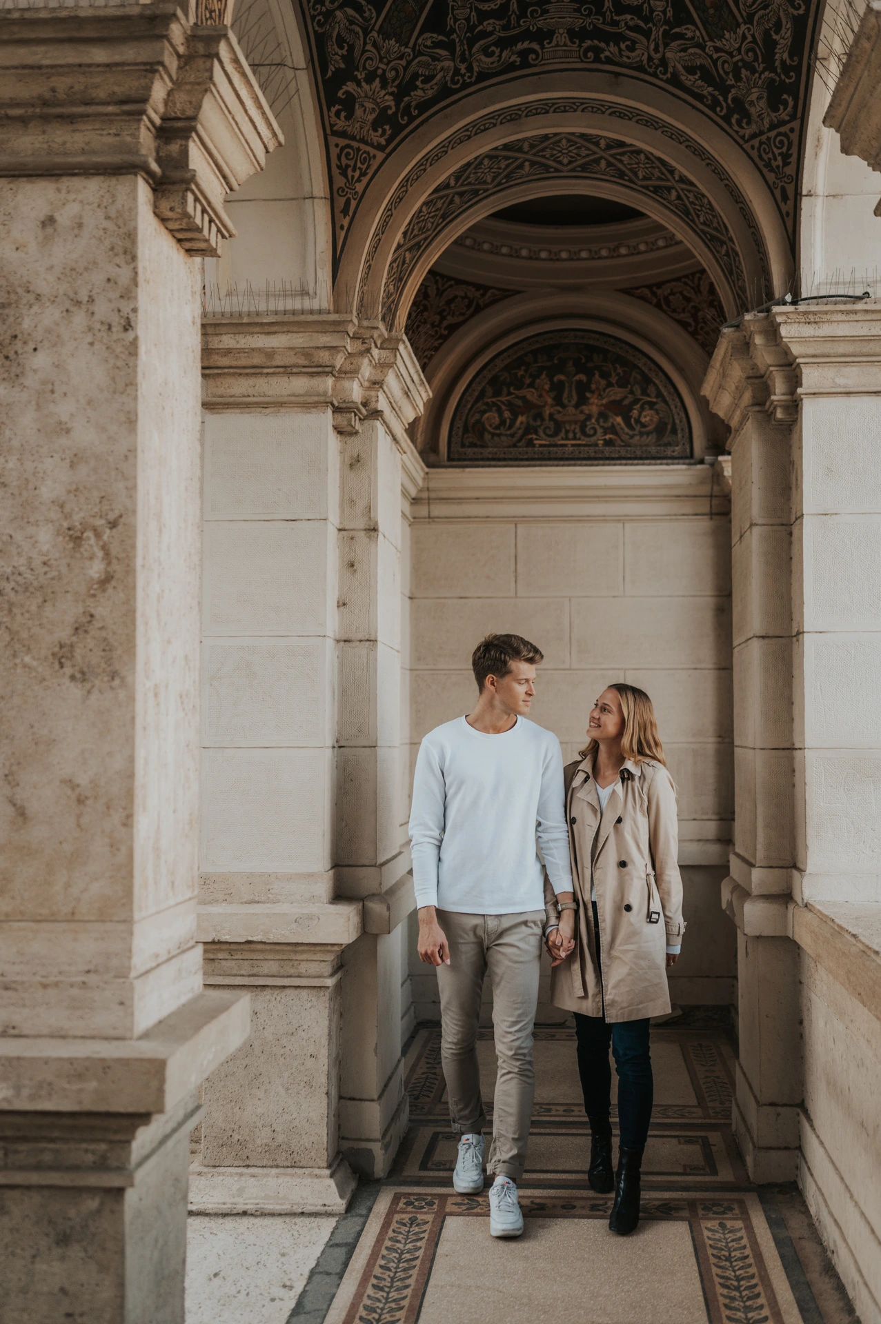 A closer portrait of the couple walking together beneath the decorated ceiling of Castle Garden Bazaar’s arched passage during their couple photoshoot in Budapest.