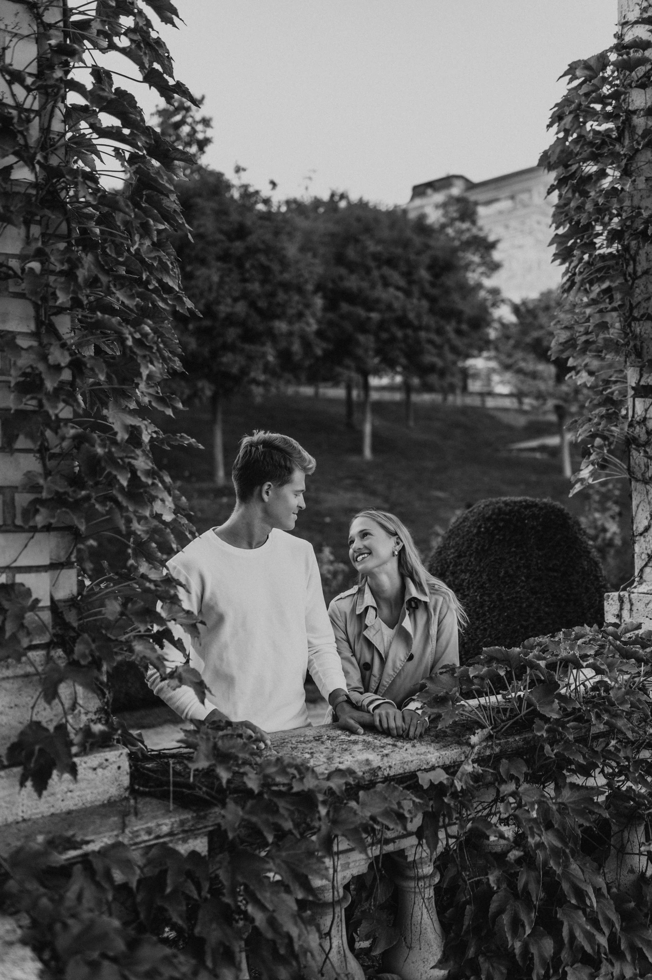 Black-and-white portrait of the couple beside an ivy-covered railing in Castle Garden Bazaar’s gardens during their couple photoshoot in Budapest.
