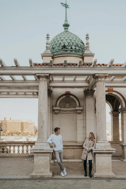 Pale stone and a green pavilion roof at a Budapest couple photoshoot The couple standing beside a stone ledge beneath Castle Garden Bazaar’s ornate pavilion and green roof during their couple photoshoot in Budapest.
