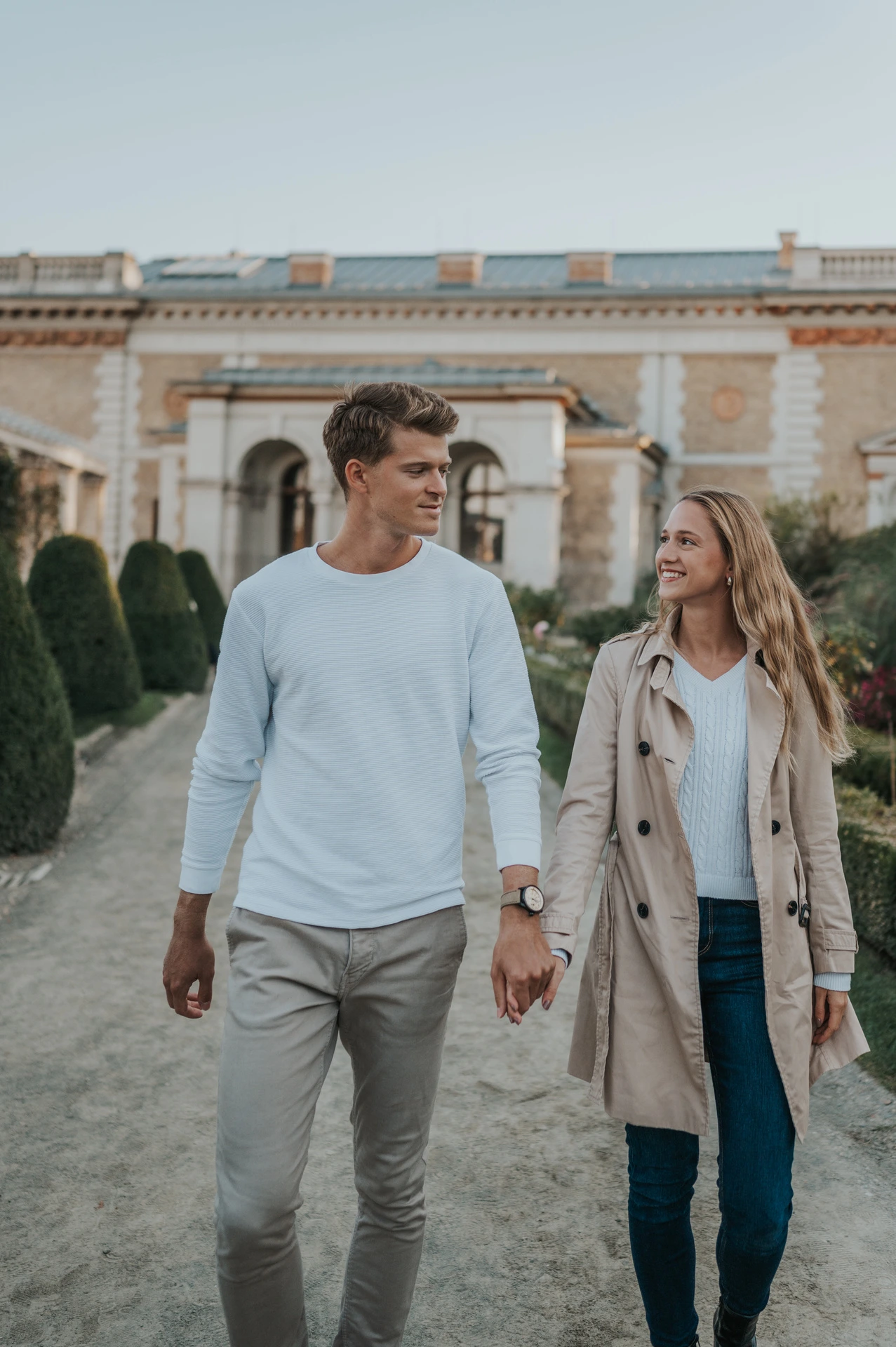 A closer portrait of the couple walking together with Castle Garden Bazaar’s pale garden pavilion behind them during their couple photoshoot in Budapest.