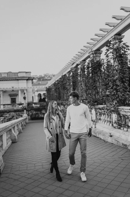 A terrace walk in black and white at a Budapest couple photoshoot Black-and-white portrait of the couple walking beside Castle Garden Bazaar’s leafy pergola during their couple photoshoot in Budapest.