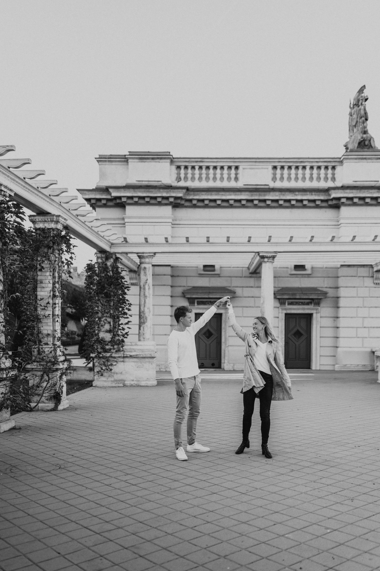 Black-and-white portrait of the couple sharing a playful turn beside Castle Garden Bazaar’s pavilion during their couple photoshoot in Budapest.