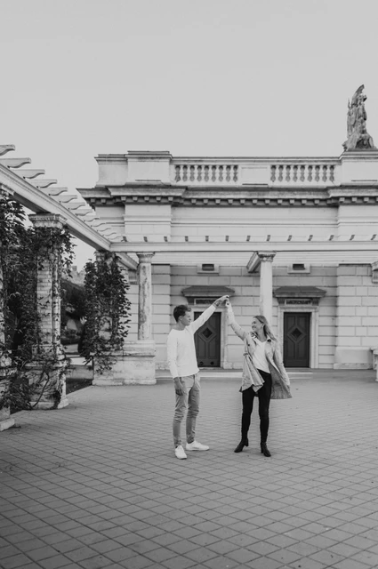 A playful pavilion portrait in black and white at a Budapest couple photoshoot Black-and-white portrait of the couple sharing a playful turn beside Castle Garden Bazaar’s pavilion during their couple photoshoot in Budapest.