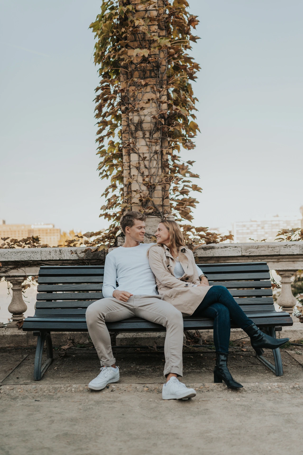 The couple sitting together on a wooden bench beneath an ivy-covered column at Castle Garden Bazaar during their couple photoshoot in Budapest.