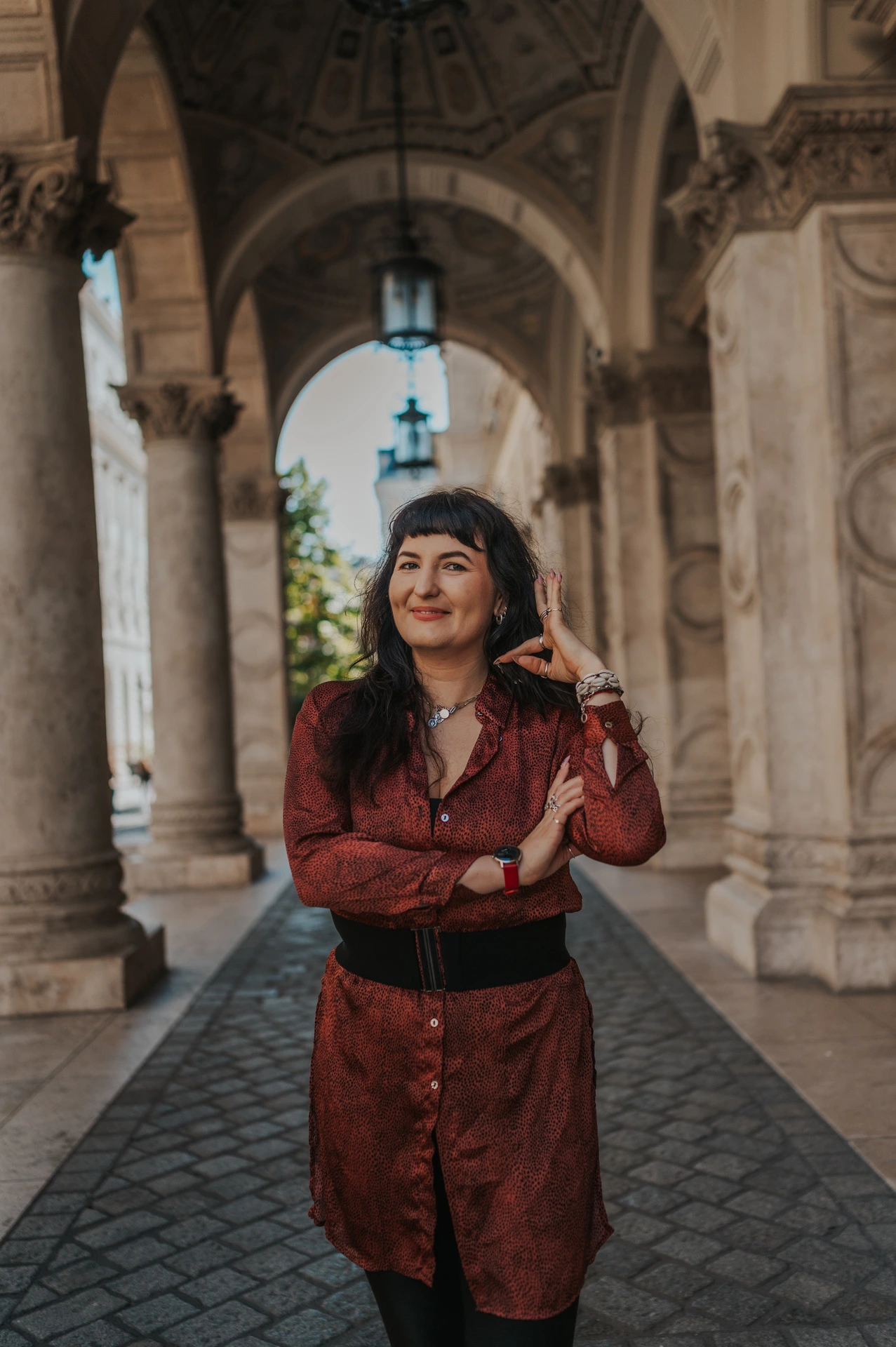 A close portrait of the woman touching her earring beneath the Opera’s stone arches during a solo photoshoot in Budapest.