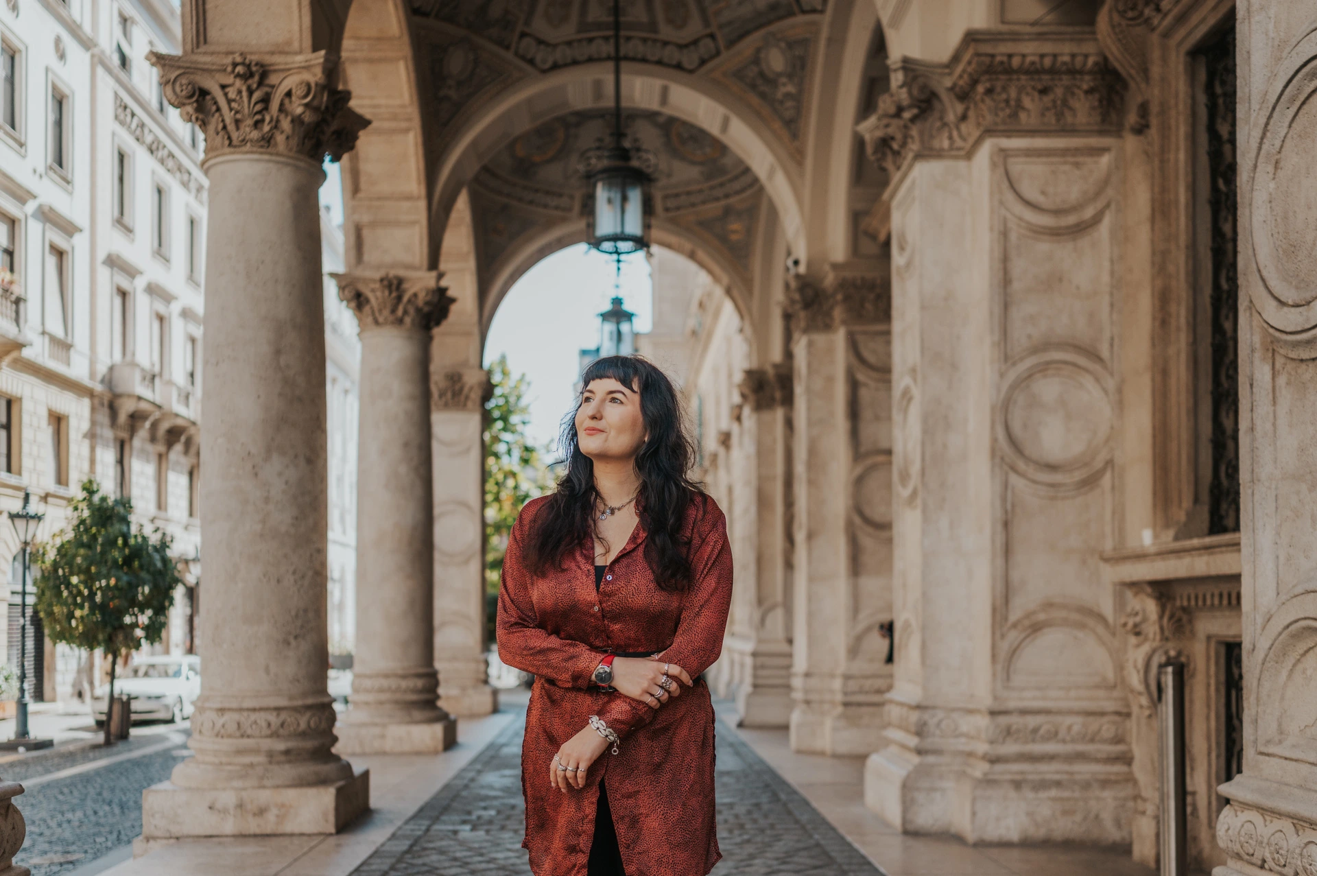 Budapest solo photoshoot: a red dress beneath the Opera arches A landscape portrait of the woman in a red dress beneath the Opera’s arches and hanging lamps during a solo photoshoot in Budapest.