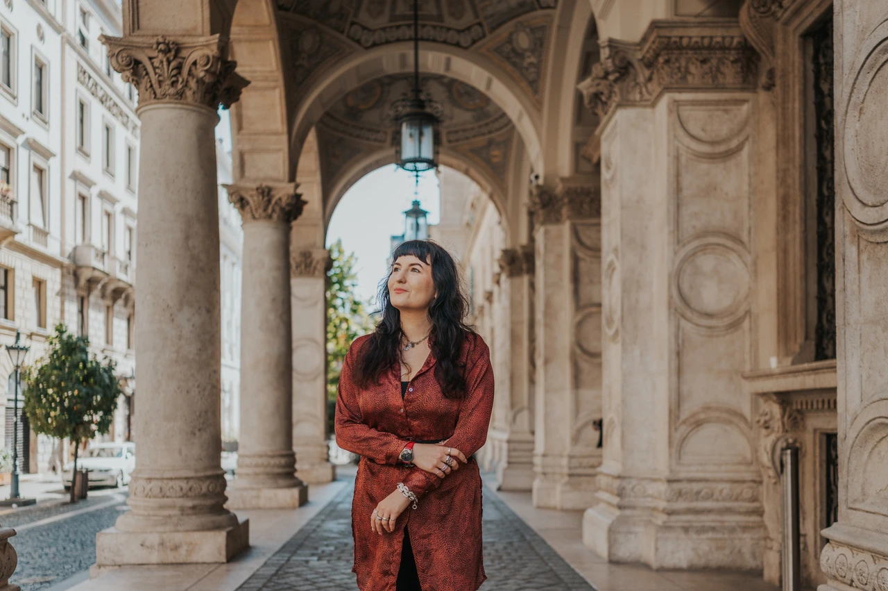 Budapest solo photoshoot: a red dress beneath the Opera arches A landscape portrait of the woman in a red dress beneath the Opera’s arches and hanging lamps during a solo photoshoot in Budapest.