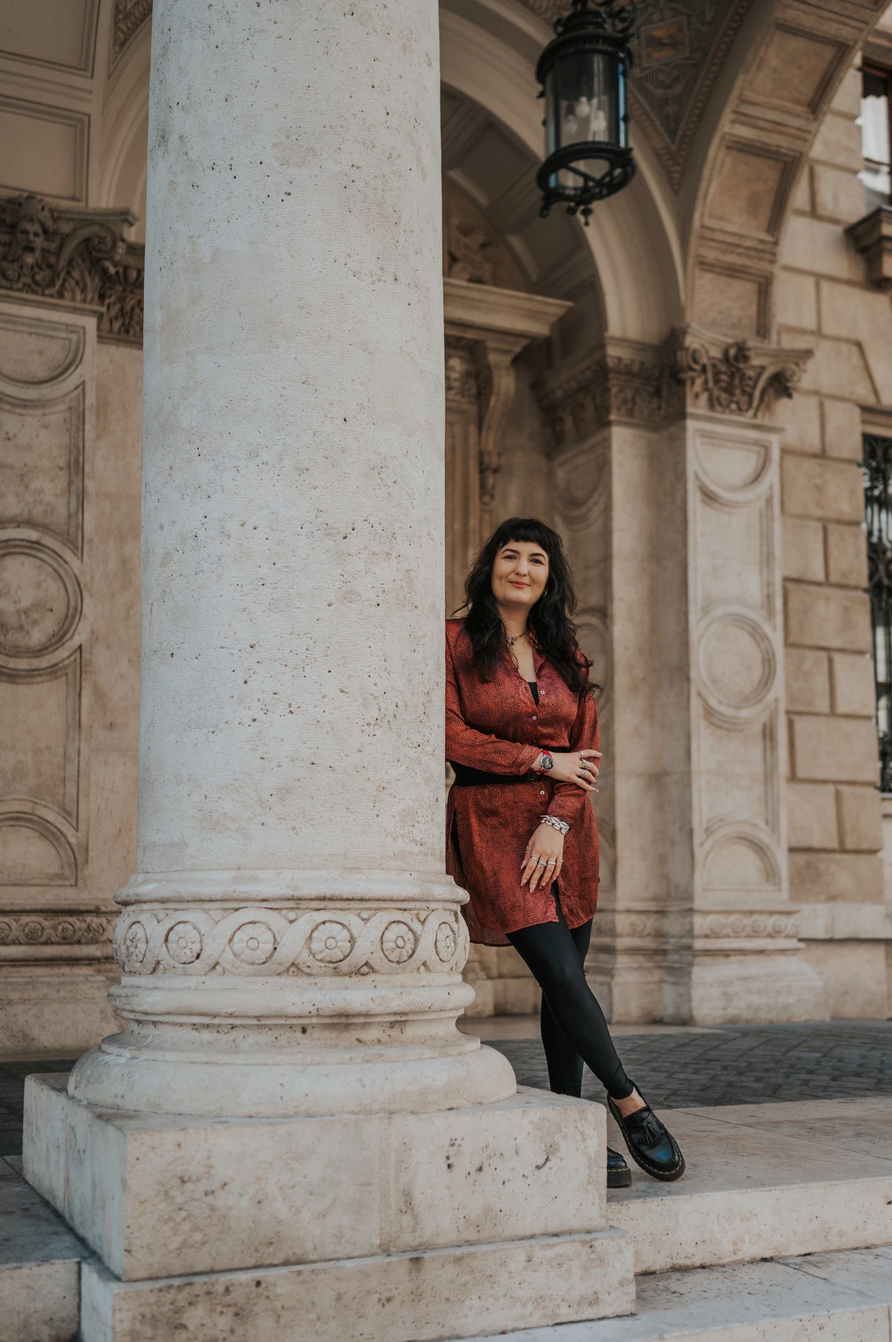 The woman leaning against a carved column beneath the Opera’s stone arches during a solo photoshoot in Budapest.