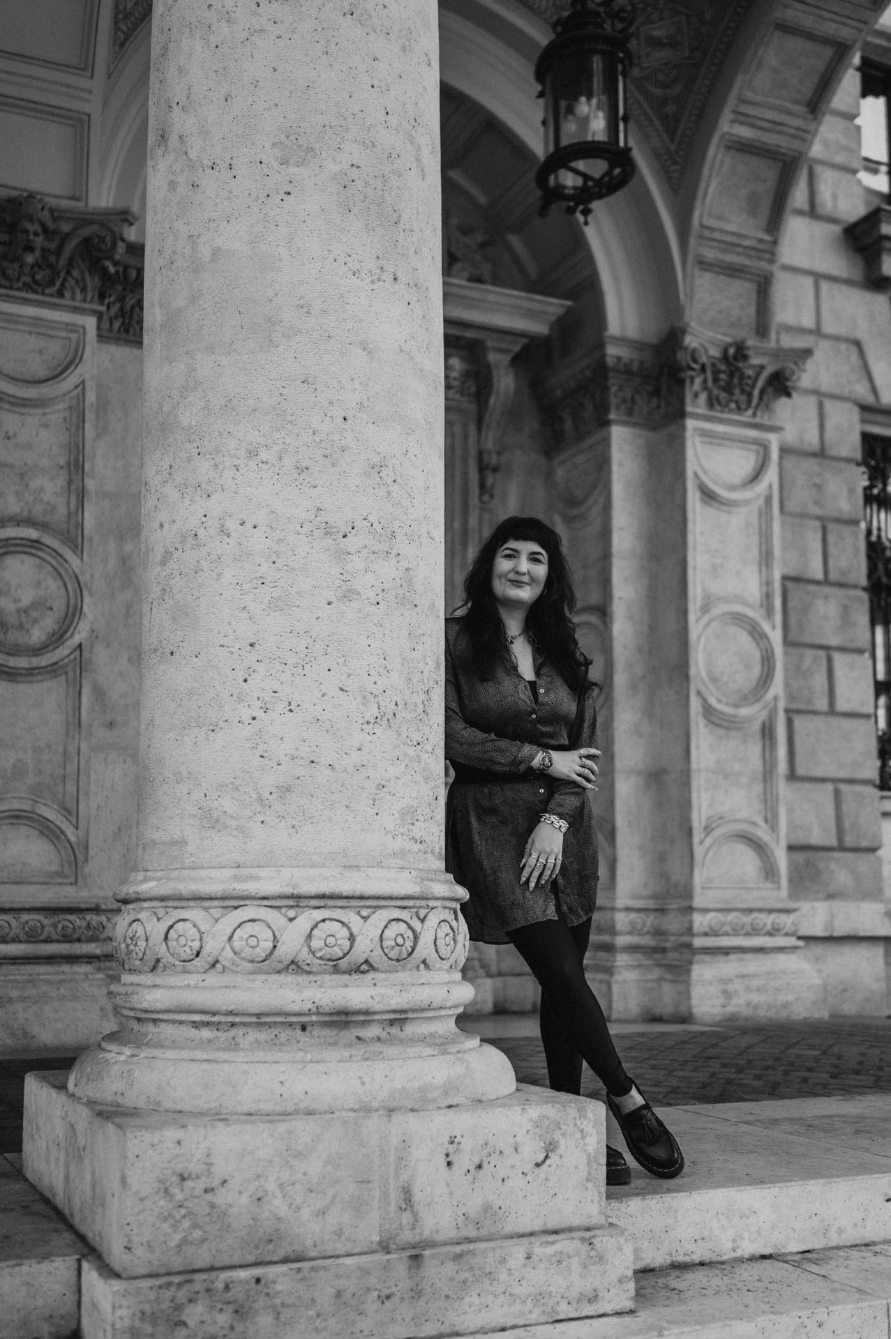 Black-and-white photograph of the woman leaning beside a large carved column outside the Opera during a solo photoshoot in Budapest.
