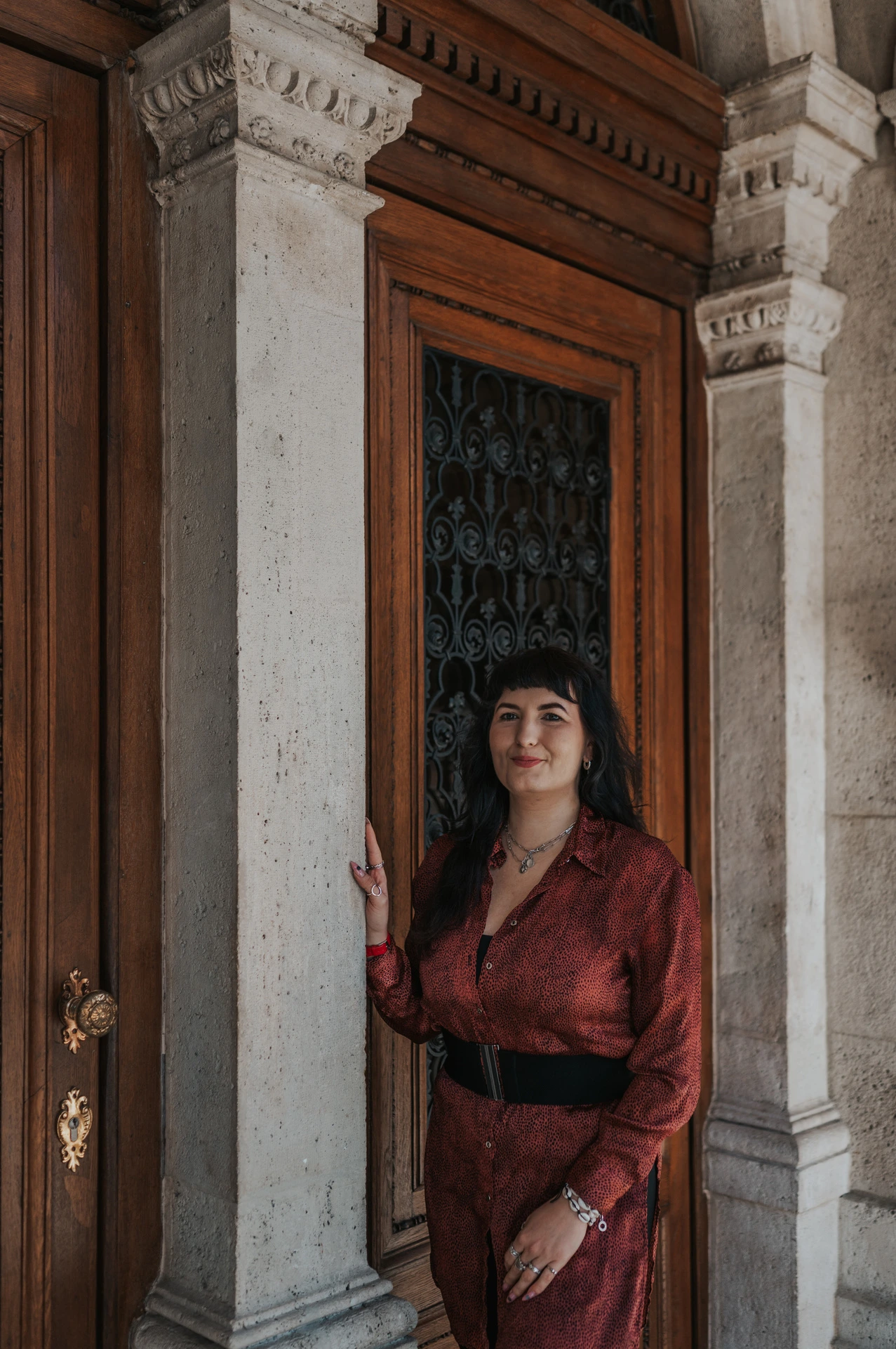 A closer portrait of the woman in a red dress at the Opera’s ornate wooden doorway during a solo photoshoot in Budapest.