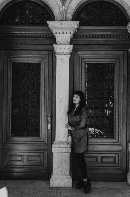 Budapest solo photoshoot: a portrait beside the carved Opera doors in black and white Black-and-white photograph of the woman looking to the side beside the Opera’s carved wooden doors and pale stone column during a solo photoshoot in Budapest.
