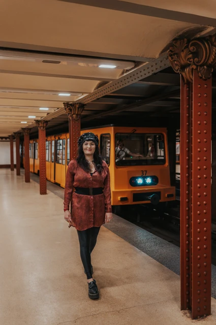 Budapest solo photoshoot: a walk along the platform beside a yellow train The woman walking along the Opera metro platform with a yellow train behind her during a solo photoshoot in Budapest.