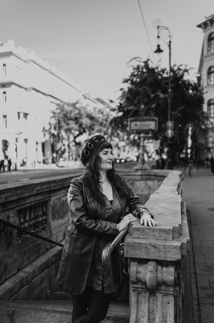 Budapest solo photoshoot: a beret and jacket by the metro balustrade in black and white Black-and-white photograph of the woman wearing a dark jacket and beret beside the stone balustrade outside Opera metro station during a solo photoshoot in Budapest.