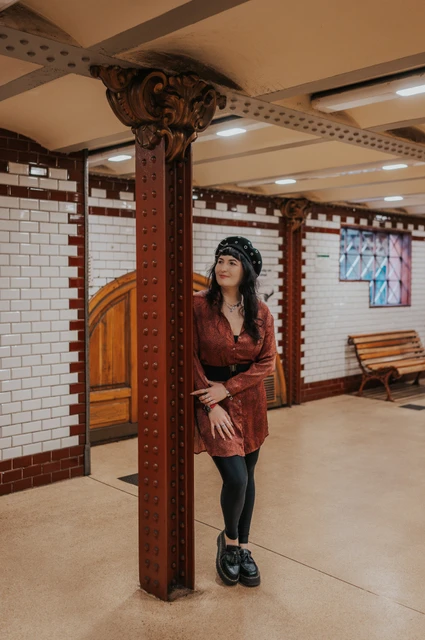 Budapest solo photoshoot: a decorative iron column on the metro platform The woman leaning beside a decorative riveted iron column on the tiled Opera metro platform during a solo photoshoot in Budapest.