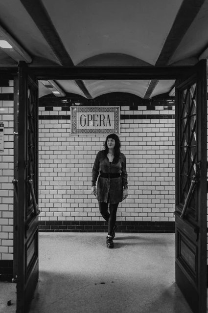 Budapest solo photoshoot: the Opera station sign and tiled walls in black and white Black-and-white photograph of the woman standing in front of a tiled wall with the Opera station sign overhead during a solo photoshoot in Budapest.