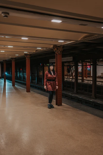 Budapest solo photoshoot: a wide view along the Opera metro platform A wide view of the woman on the Opera metro platform with a line of iron columns beside the tracks during a solo photoshoot in Budapest.
