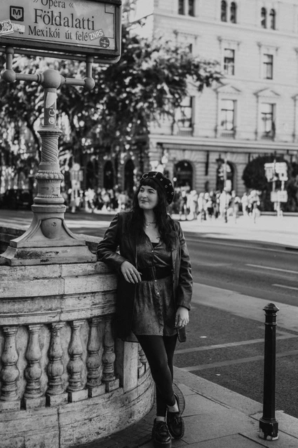 Budapest solo photoshoot: a portrait beside the Földalatti sign in black and white Black-and-white photograph of the woman in a beret and jacket leaning beside the stone balustrade and Földalatti sign at Opera station during a solo photoshoot in Budapest.