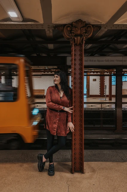 Budapest solo photoshoot: a passing yellow train at Opera station The woman beside a riveted iron column as a yellow train passes through Opera metro station during a solo photoshoot in Budapest.