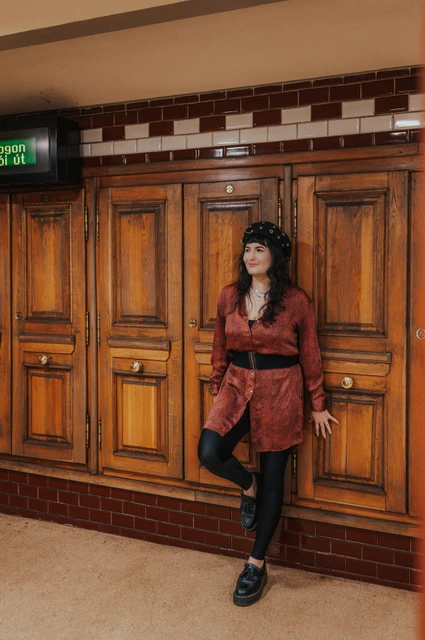 Budapest solo photoshoot: red tones against the metro’s wooden panelling The woman in a red dress leaning against wooden panelling inside Opera metro station during a solo photoshoot in Budapest.