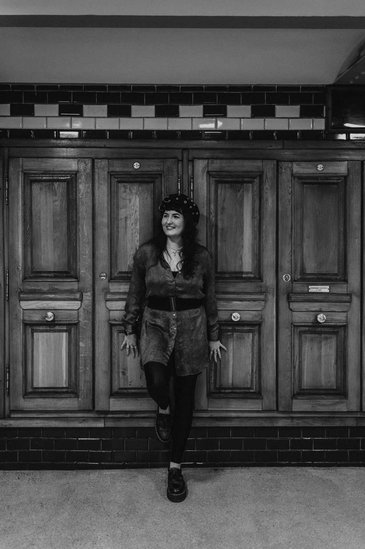 Black-and-white photograph of the woman leaning beside the wood-panelled wall inside Opera metro station during a solo photoshoot in Budapest.