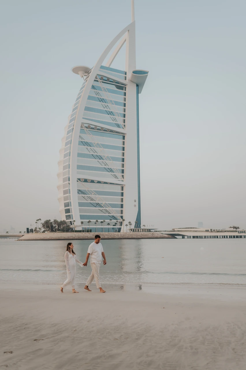 Burj Al Arab maternity photoshoot Dubai - walking silhouette An expecting couple walks across wet sand in Dubai with Burj Al Arab behind them during a maternity photoshoot at golden hour.