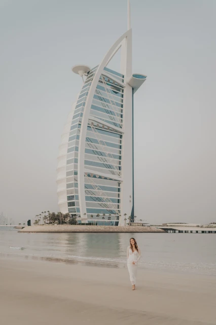 Burj Al Arab maternity photoshoot Dubai - hero portrait A pregnant woman stands on Dubai beach with Burj Al Arab visible behind her during a maternity photoshoot at soft golden hour.