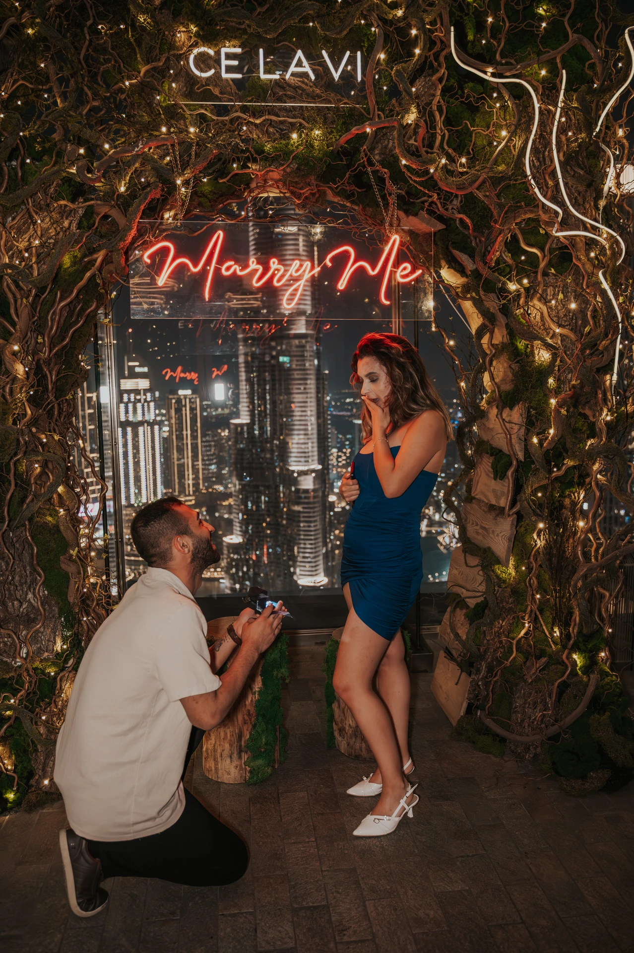 CE LA VI rooftop proposal Dubai - Kneeling Proposal Setup A man kneels to propose at CE LA VI rooftop in Dubai while his partner stands surprised beneath the illuminated “Marry Me” sign.
