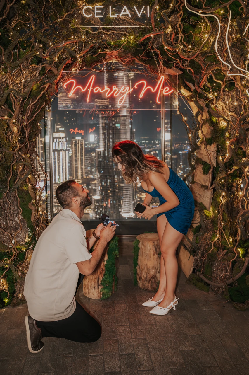 CE LA VI rooftop proposal Dubai - Surprise Ring Moment A man kneels with a ring box during a CE LA VI rooftop proposal in Dubai as his partner reacts under a neon “Marry Me” sign.