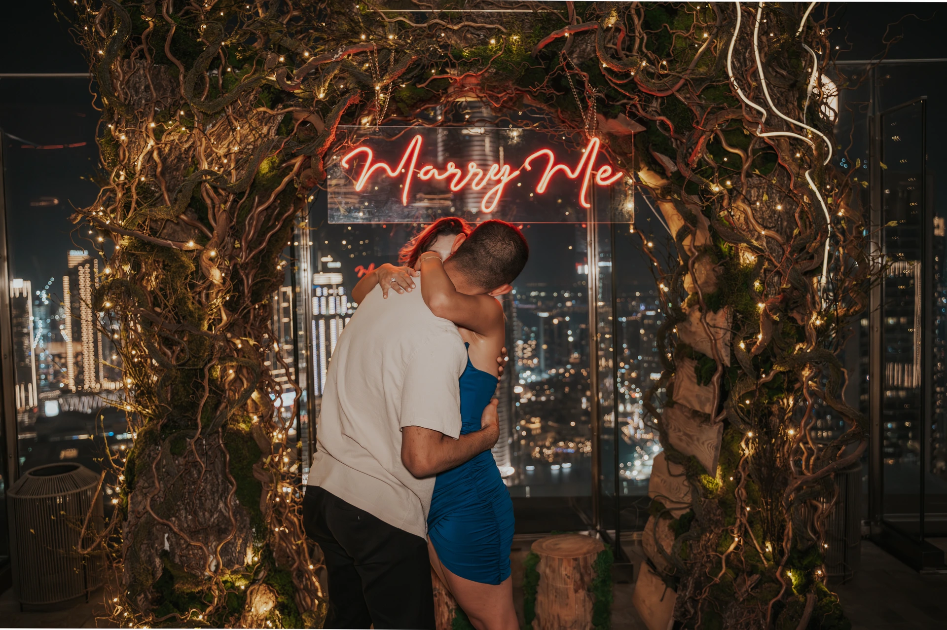 A couple embraces after saying yes during a CE LA VI rooftop proposal in Dubai, framed by a glowing “Marry Me” sign.
