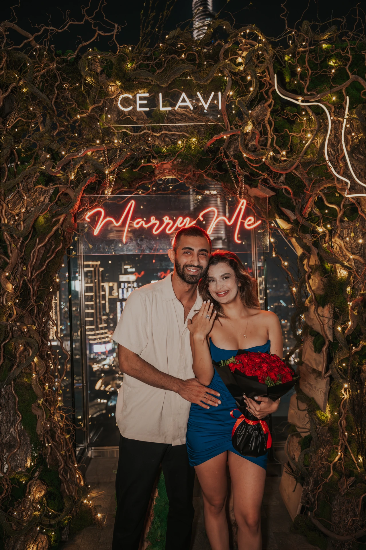 CE LA VI rooftop proposal Dubai - Ring and Roses Portrait A newly engaged couple smiles at CE LA VI in Dubai, with the engagement ring visible and a bouquet of red roses in hand.