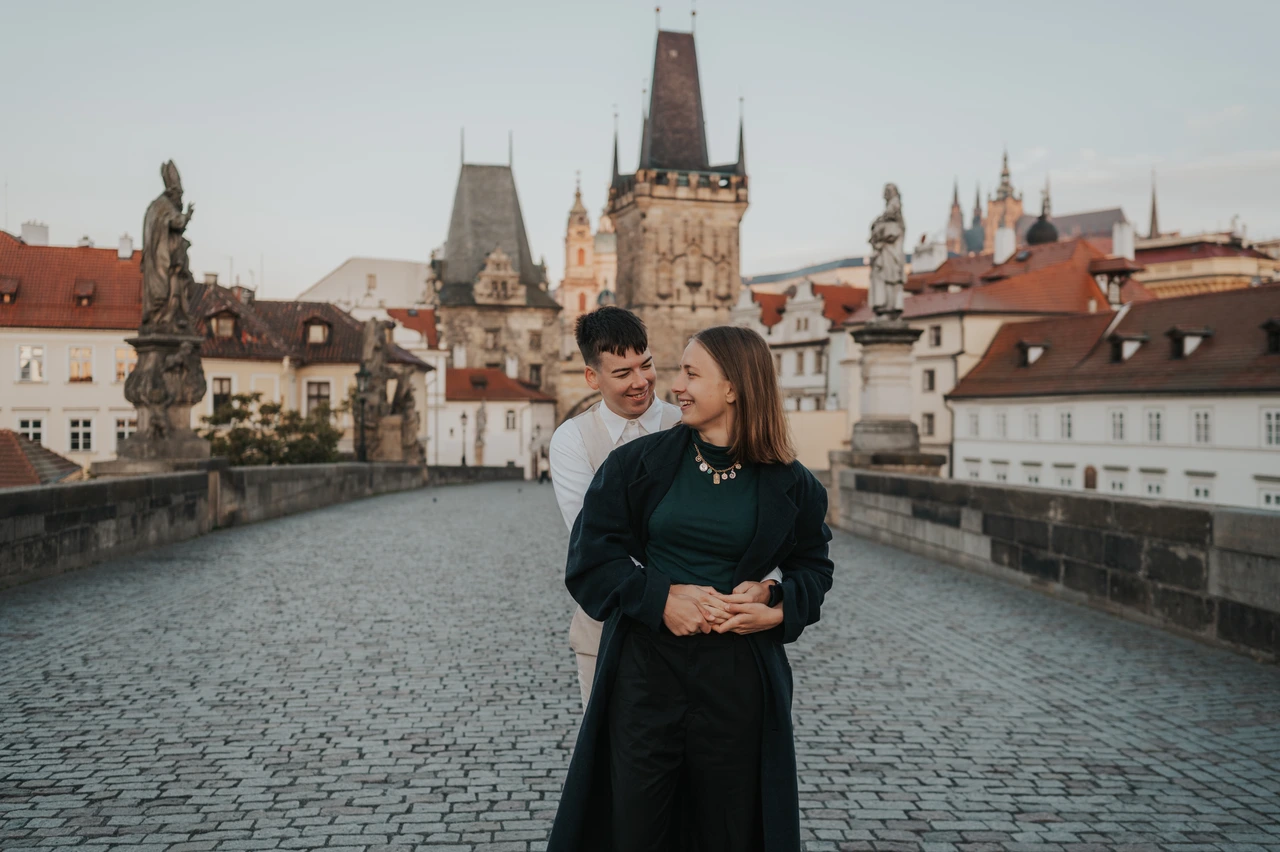 Charles Bridge Photos - Couple and Lesser Town Towers A couple hold each other on Charles Bridge, with the Lesser Town Bridge Towers and red rooftops behind them.